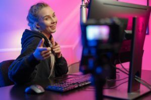 Funny and smiling e-sport gamer girl vlogging and plays online video game on PC
