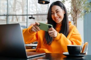 Smiling asian woman playing online game on cellphone in cafe