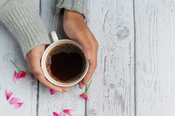 Two people holding cup of coffee in hands with love and warmth on wooden table